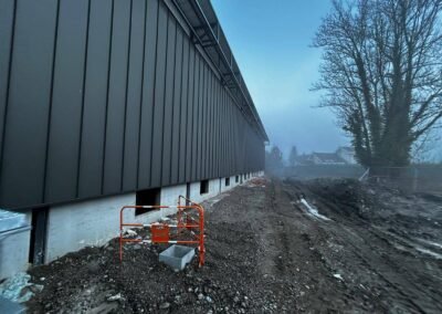 Vue latérale longue façade bardage métallique anthracite avec chantier en cours et accès chantier sécurisé